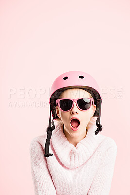 Buy stock photo Shot of an attractive young woman sitting alone in the studio and looking shocked while wearing a helmet and sunglasses