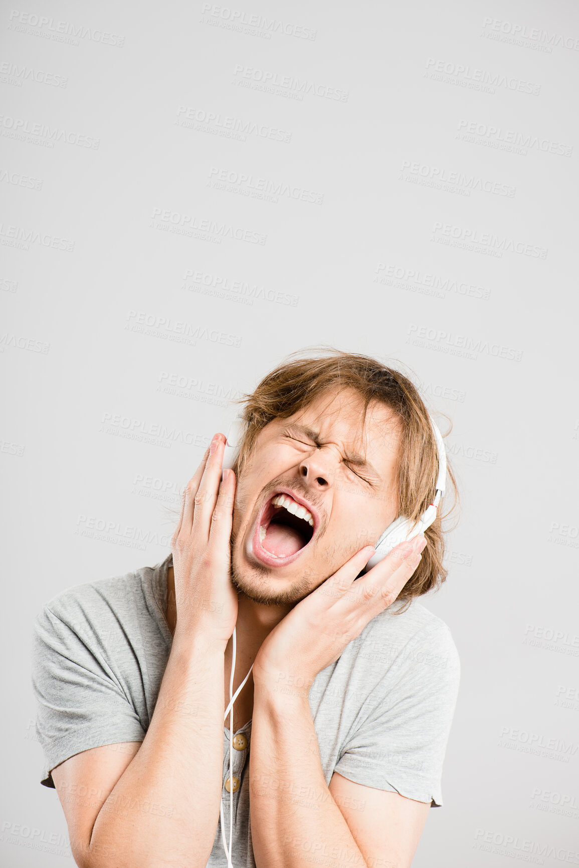 Buy stock photo Shot of a handsome young man standing alone in the studio and listening to music through headphones