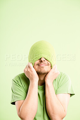 Buy stock photo Funny, face and man in studio with beanie, smile and comedy with happy aesthetic style on mockup. Shy, hiding and gen z person with positive attitude, joke and casual fashion on green background.