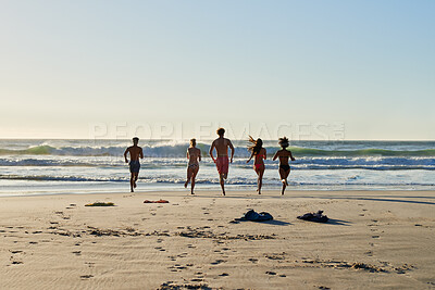 Buy stock photo Shot of a group of friends running into the water at the beach