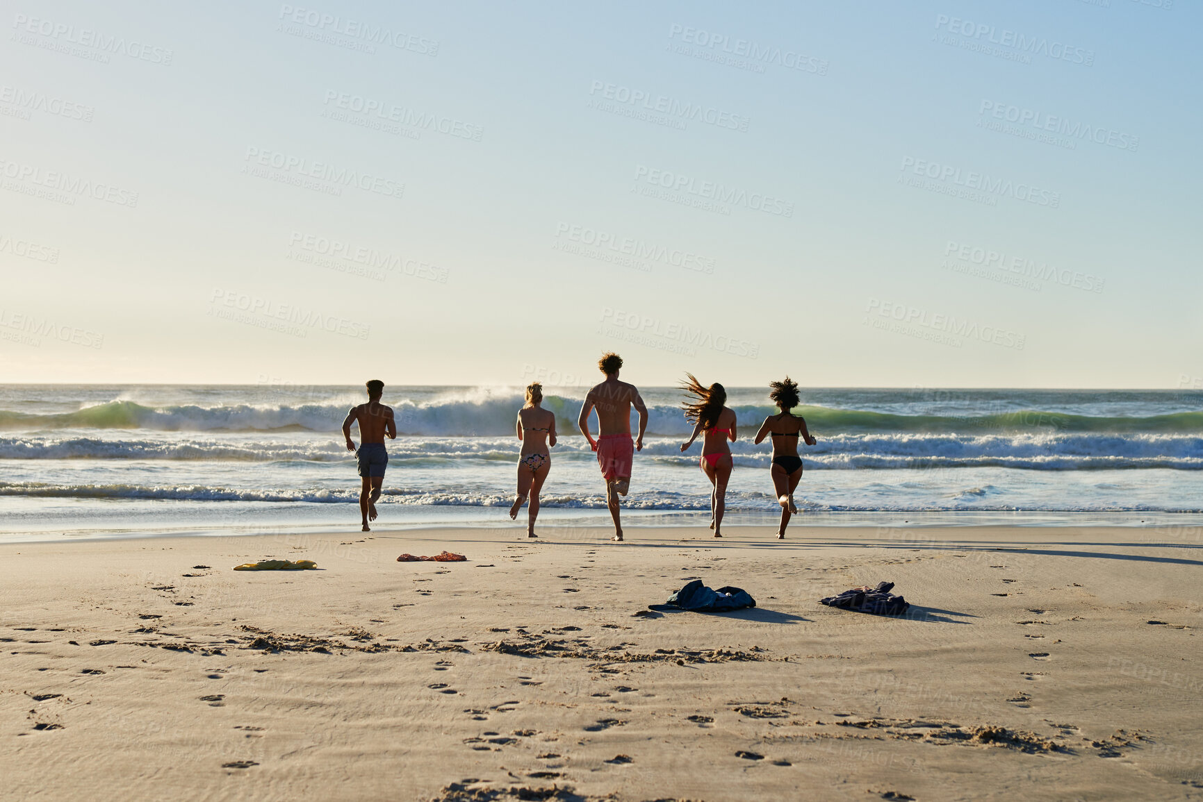 Buy stock photo Shot of a group of friends running into the water at the beach