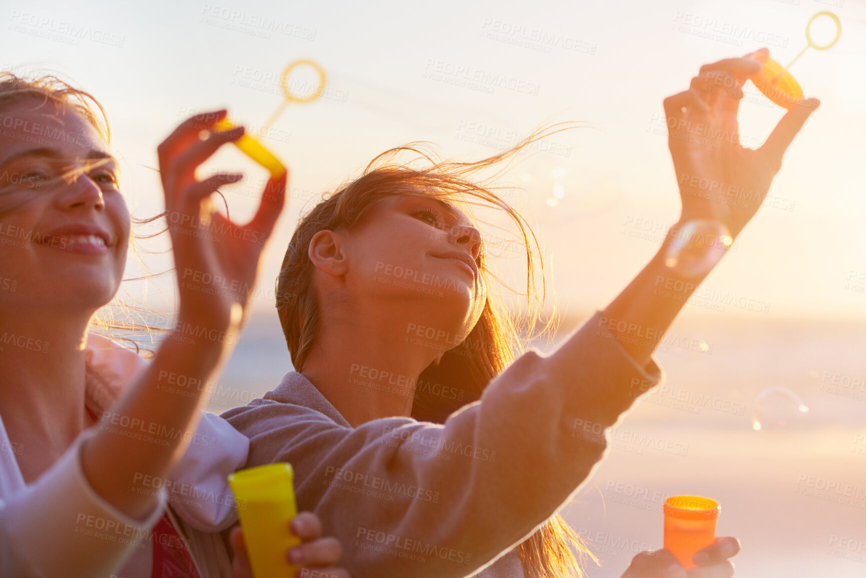 Buy stock photo Girl, friends and bubbles at beach, sunset and happy on vacation with game, bonding and playful in summer. Women, smile and plastic container for soap, foam and liquid on holiday by sea in Portugal