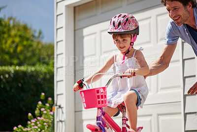 Buy stock photo Child learning from dad to ride a bicycle as support, trust and skill development outdoor of a home or house together. Parent, safety and happy father care, help and teaching kid or girl to use bike