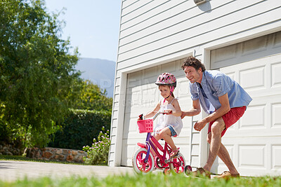 Buy stock photo Father teaching child to ride a bike as support, trust and skill development outdoor of a home or house together. Parent, safety and happy dad care and help kid or girl learning to use a bicycle