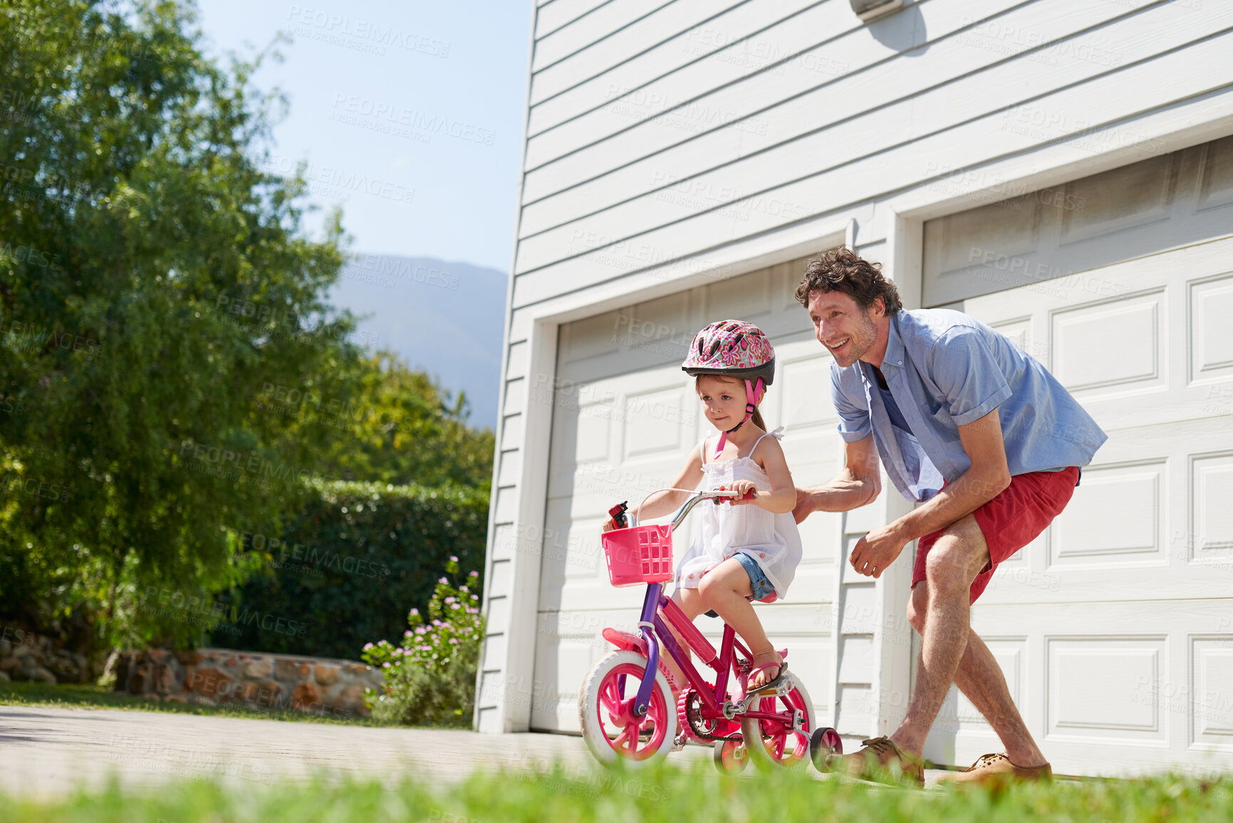 Buy stock photo Father teaching child to ride a bike as support, trust and skill development outdoor of a home or house together. Parent, safety and happy dad care and help kid or girl learning to use a bicycle