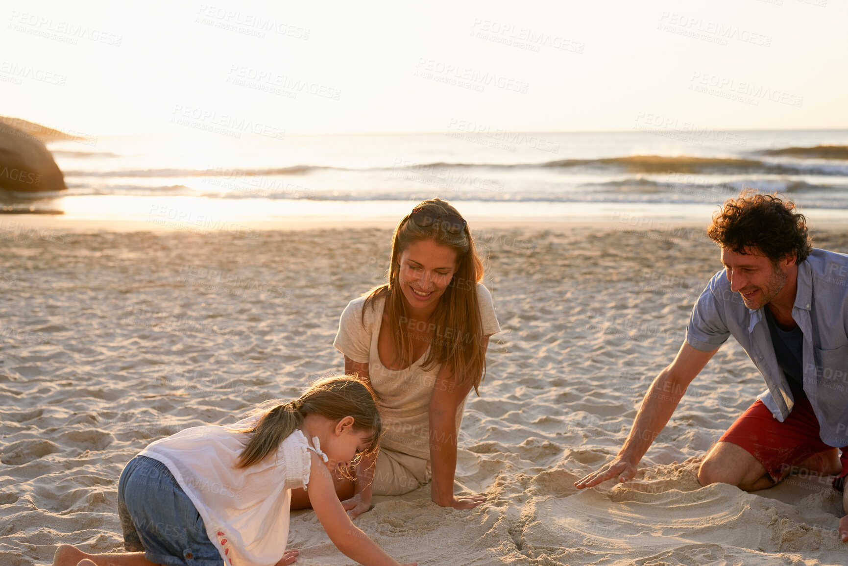 Buy stock photo Parents, girl and child at beach with sandcastle, playful and bonding with smile, love and outdoor on vacation. Father, mother and daughter with care, digging and relax by ocean at sunset in Spain