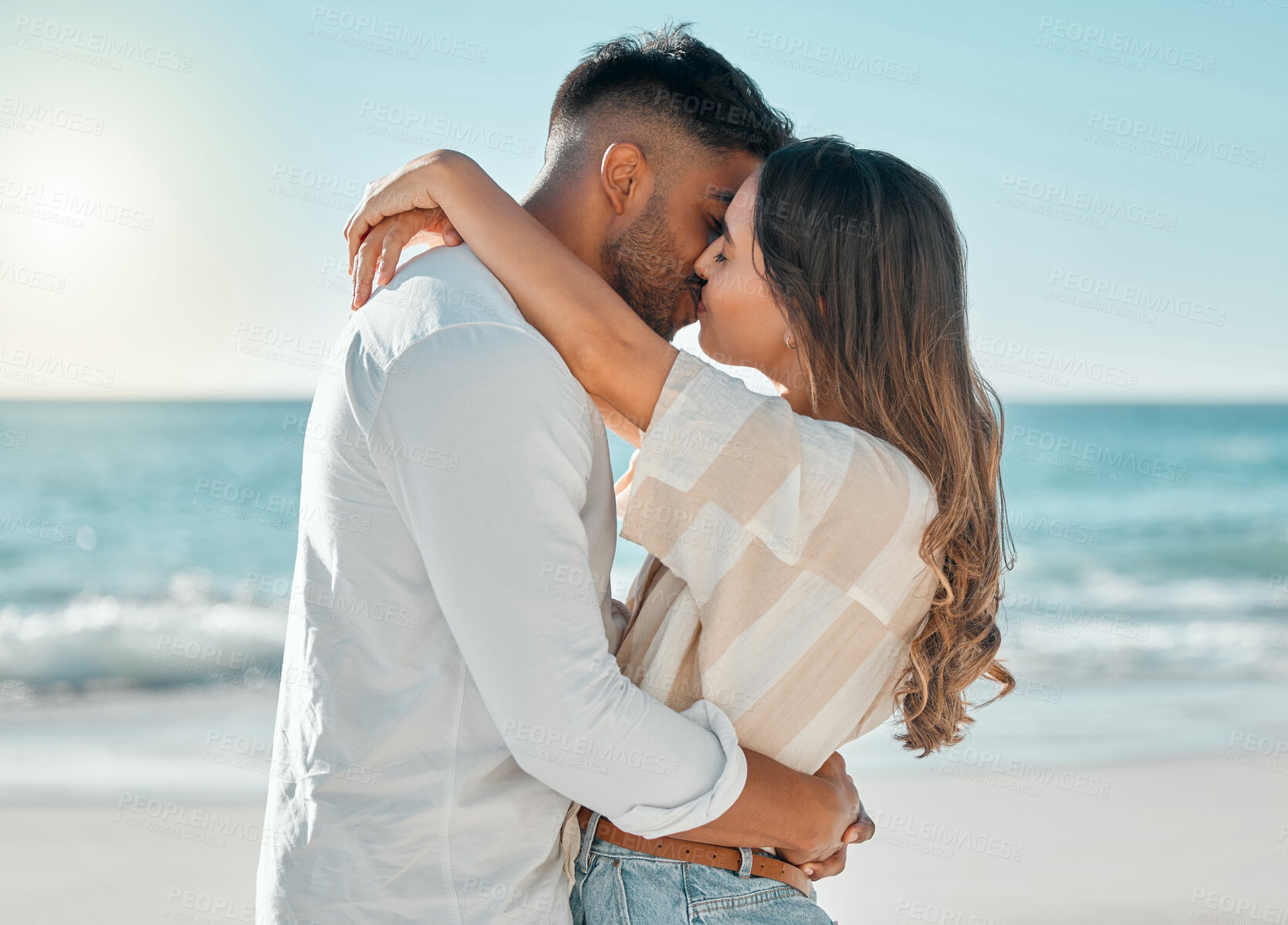 Buy stock photo Shot of a young couple kissing while spending a day at the beach