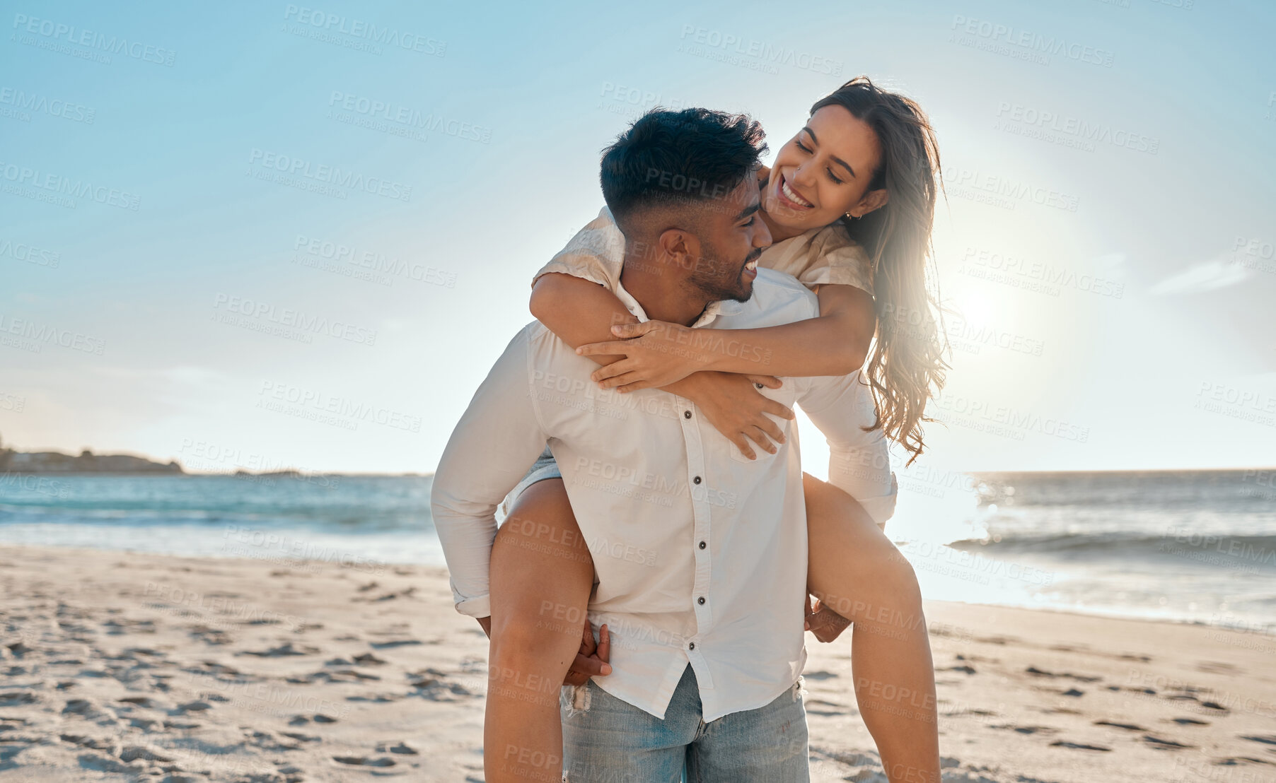 Buy stock photo Piggyback, happy and couple by beach on holiday, getaway or vacation with travel together. Smile, love and interracial man and woman with playful romance by ocean or sea on date on weekend trip.