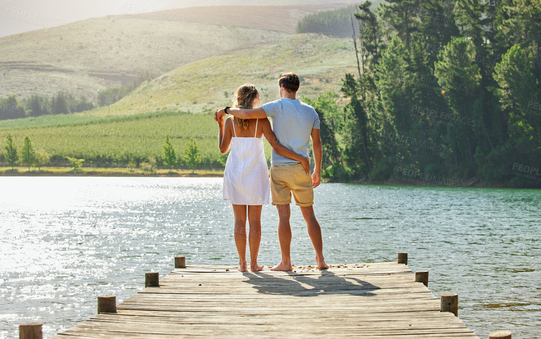 Buy stock photo Couple on jetty by the lake, travel and relax together with nature and hug outdoor, love with care and bonding. Summer, holiday with man and woman back view, sunshine and relationship with trust