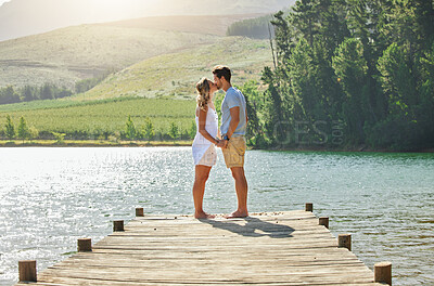 Buy stock photo Couple, kissing and holding hands by the lake in romance for love, care and affection together in nature. Man and woman kiss by water on a romantic getaway, summer vacation or date by the lakeside