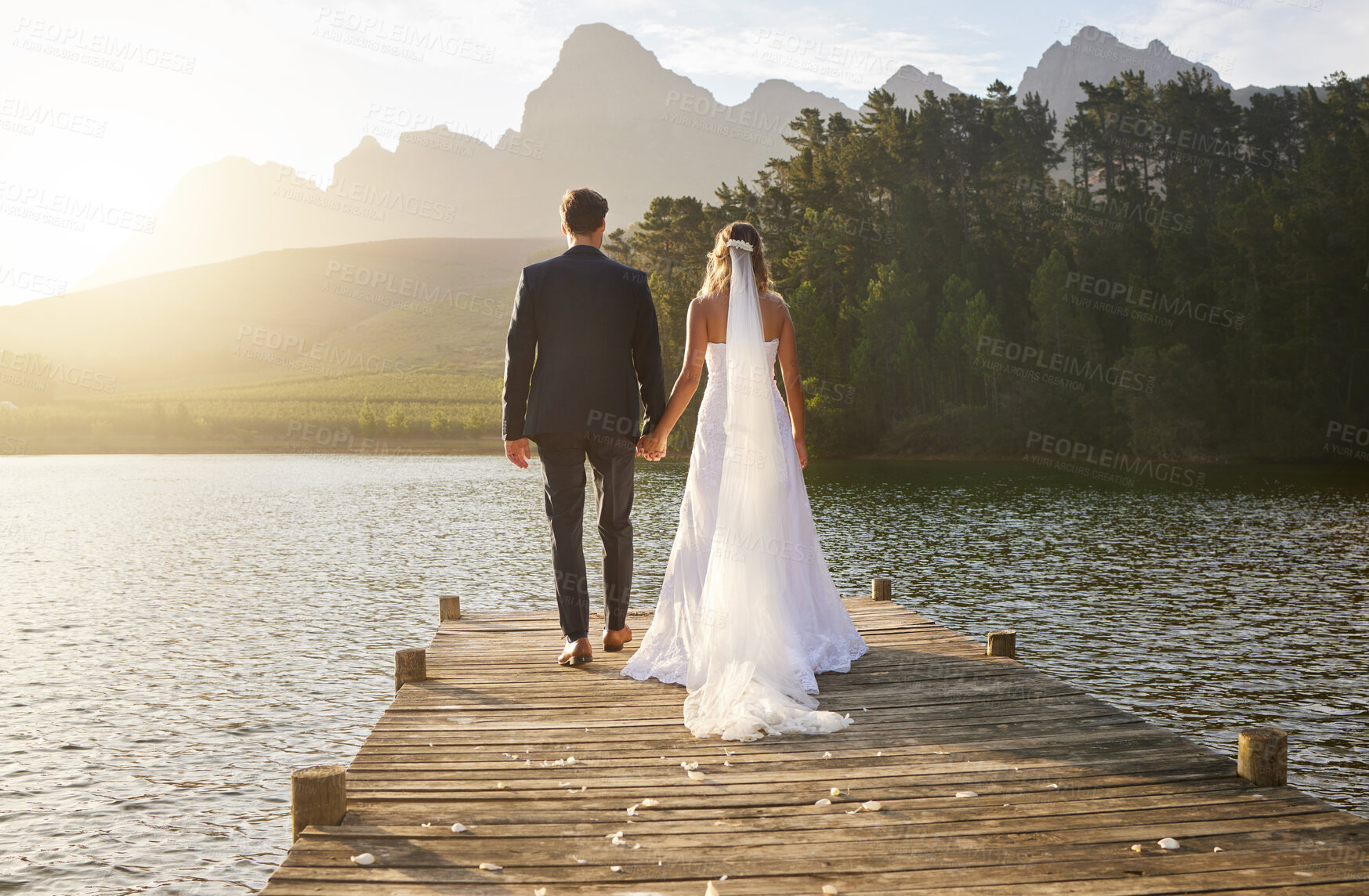 Buy stock photo Love, wedding and back of couple by a lake standing, bonding and holding hands on the pier. Nature, romance and young bride and groom in an intimate moment together outdoor on a romantic marriage day