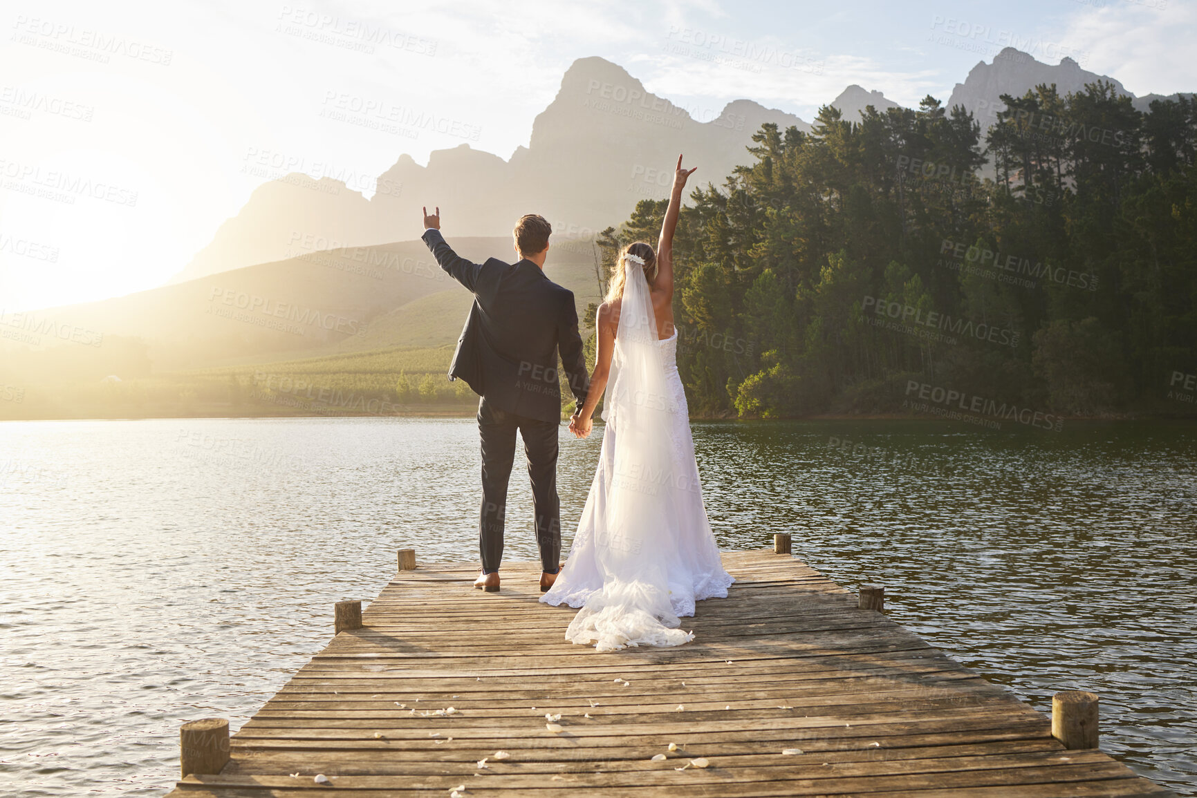 Buy stock photo Love, hand signs and couple by a lake for their wedding standing, bonding and holding hands on the pier. Nature, romance and young bride and groom in funny moment together on a romantic marriage day.