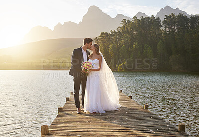 Buy stock photo Kiss, romantic and a married couple on a pier over a lake in nature with a forest in the background after a ceremony. Wedding, love or water with a bride and groom in celebration of marriage outdoor