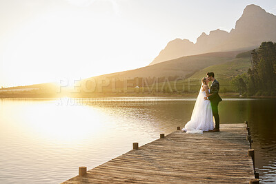 Buy stock photo Kiss, sunset and married couple by a lake for a wedding, marriage ceremony and event. Together, happy and a bride and groom standing by a pier, kissing and giving affection to celebrate their love