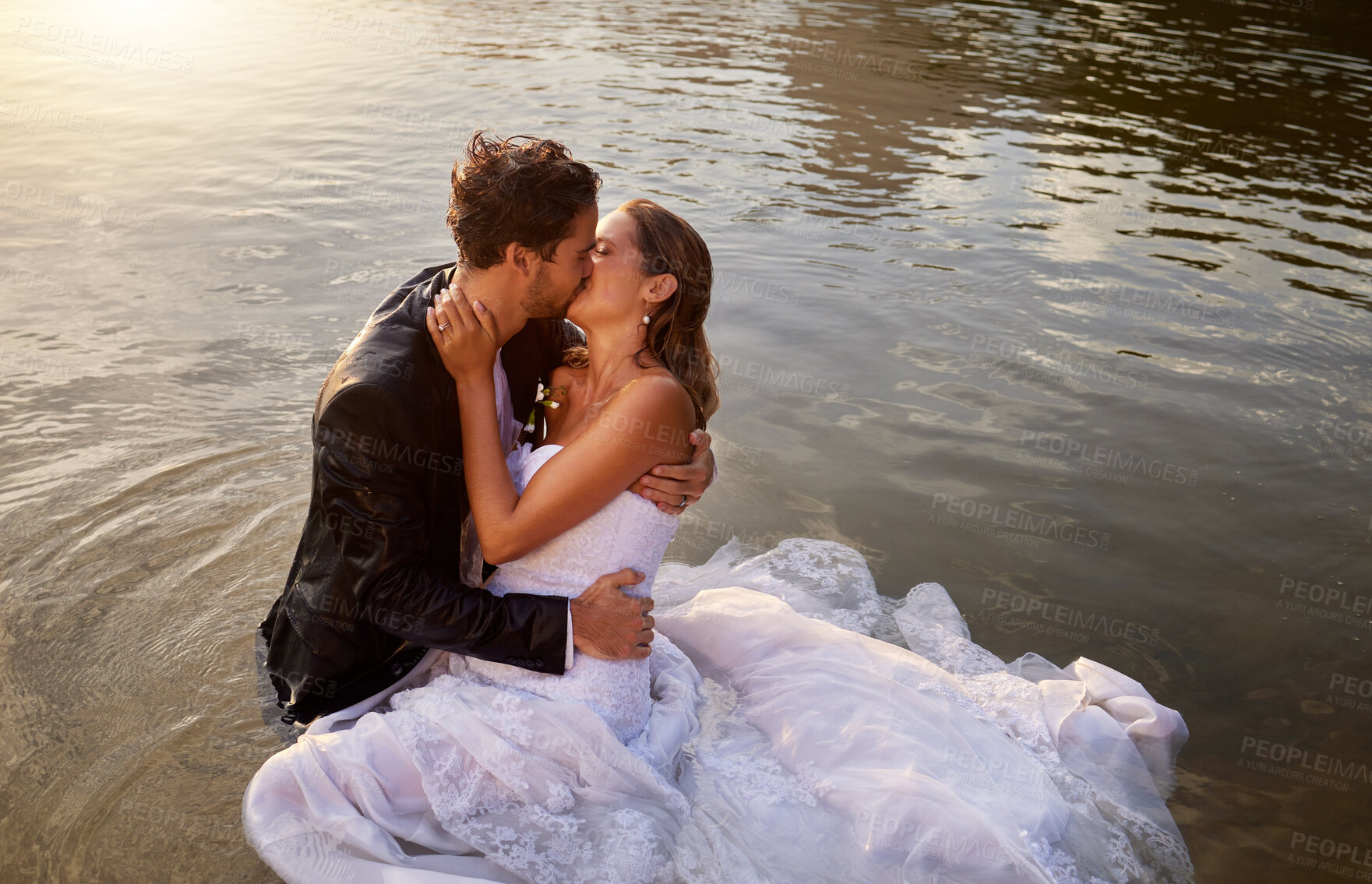 Buy stock photo Wedding, kiss and couple in the water of a lake to celebrate their sunset marriage outdoor in nature. Happy, love and young wet man and woman being intimate for romantic playful outdoor celebration.