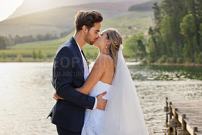 Buy stock photo Love, wedding and a married couple kissing by a lake outdoor in celebration of their marriage for romance. Water, summer or kiss with a bride and groom bonding together in tradition after ceremony