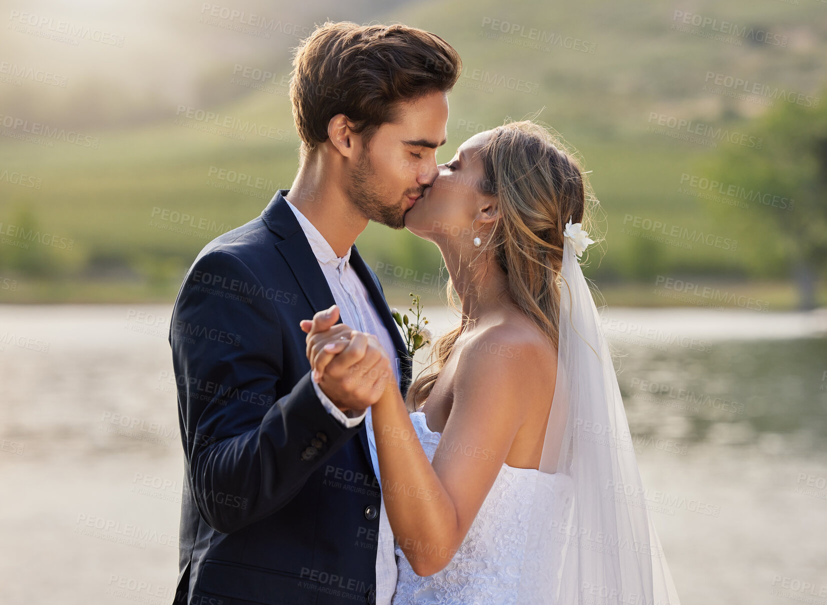 Buy stock photo Wedding kiss, couple and lake with a bride feeling love, care and support from marriage together. Nature, happiness and holding hands of young people with romance from trust and commitment event