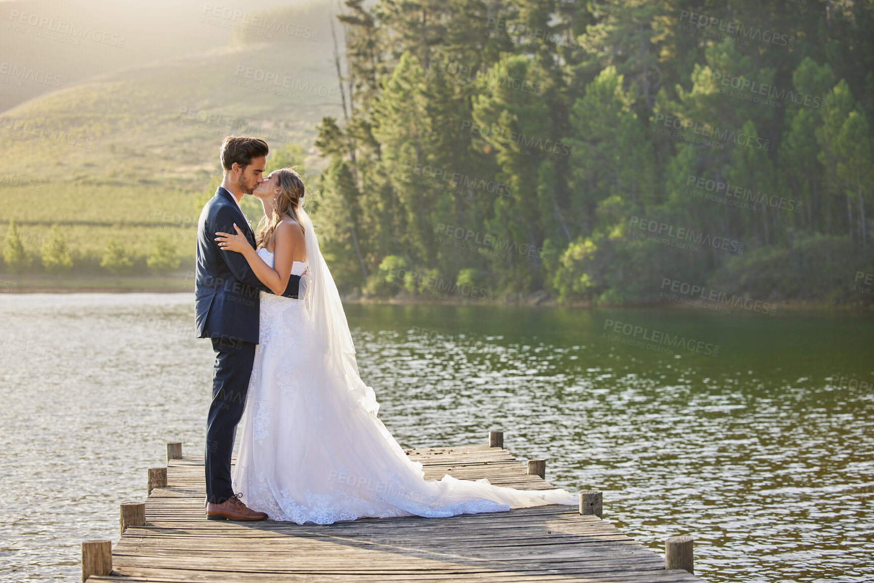 Buy stock photo Wedding couple, kissing and hug by lake for love affection, intimate or romantic honeymoon getaway in nature. Man and woman kiss in happiness for marriage relationship or loving embrace outdoors