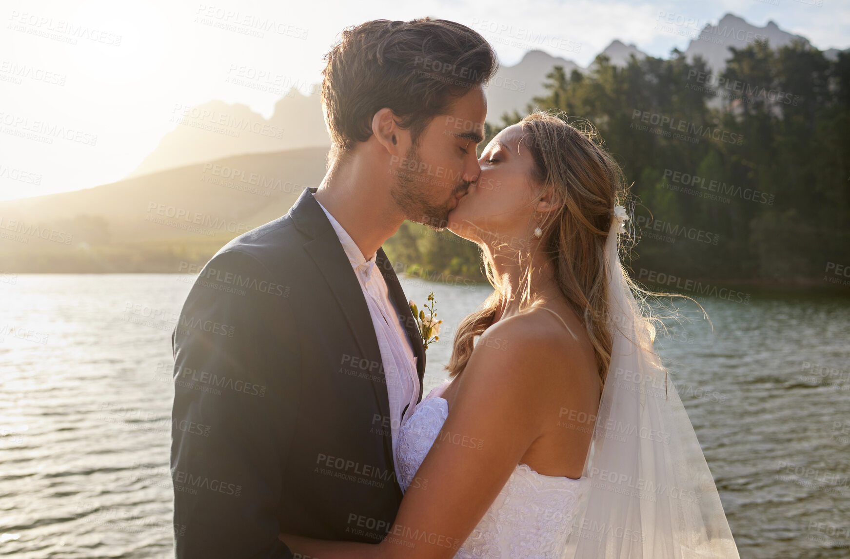 Buy stock photo Love, wedding and a newlywed couple kissing by a lake outdoor in celebration of their marriage for romance. Water, summer or kiss with a bride and groom bonding together in tradition after ceremony