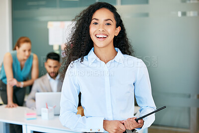 Buy stock photo Shot of a young businesswoman standing in the office and holding a digital tablet while her colleagues work behind her