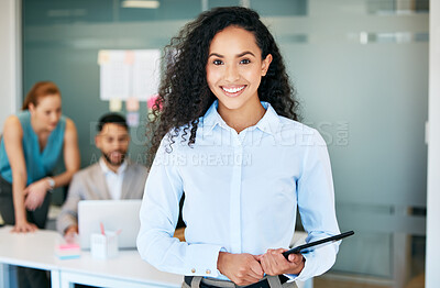 Buy stock photo Shot of a young businesswoman standing in the office and holding a digital tablet while her colleagues work behind her