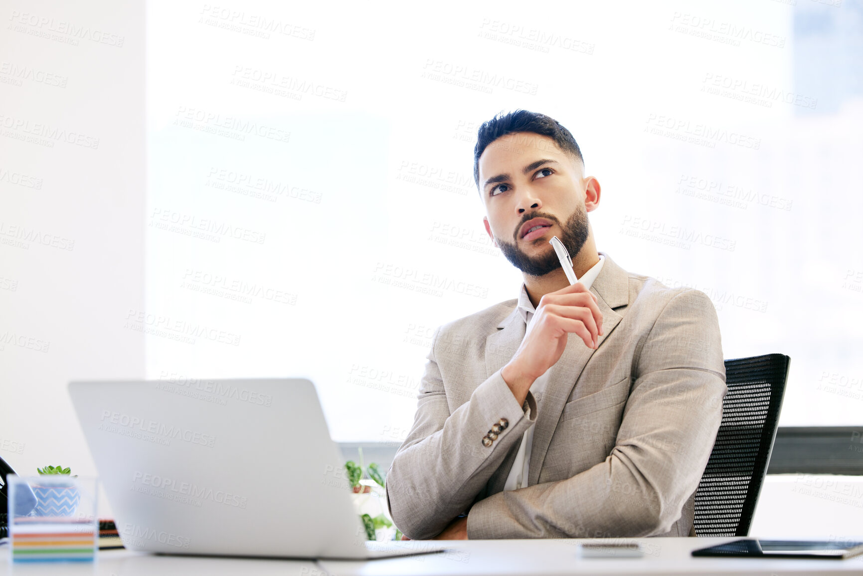 Buy stock photo Shot of a handsome young businessman sitting alone in the office and looking contemplative using his laptop