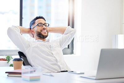 Buy stock photo Shot of a handsome young businessman sitting alone in the office with his hands behind his head and feeling successful