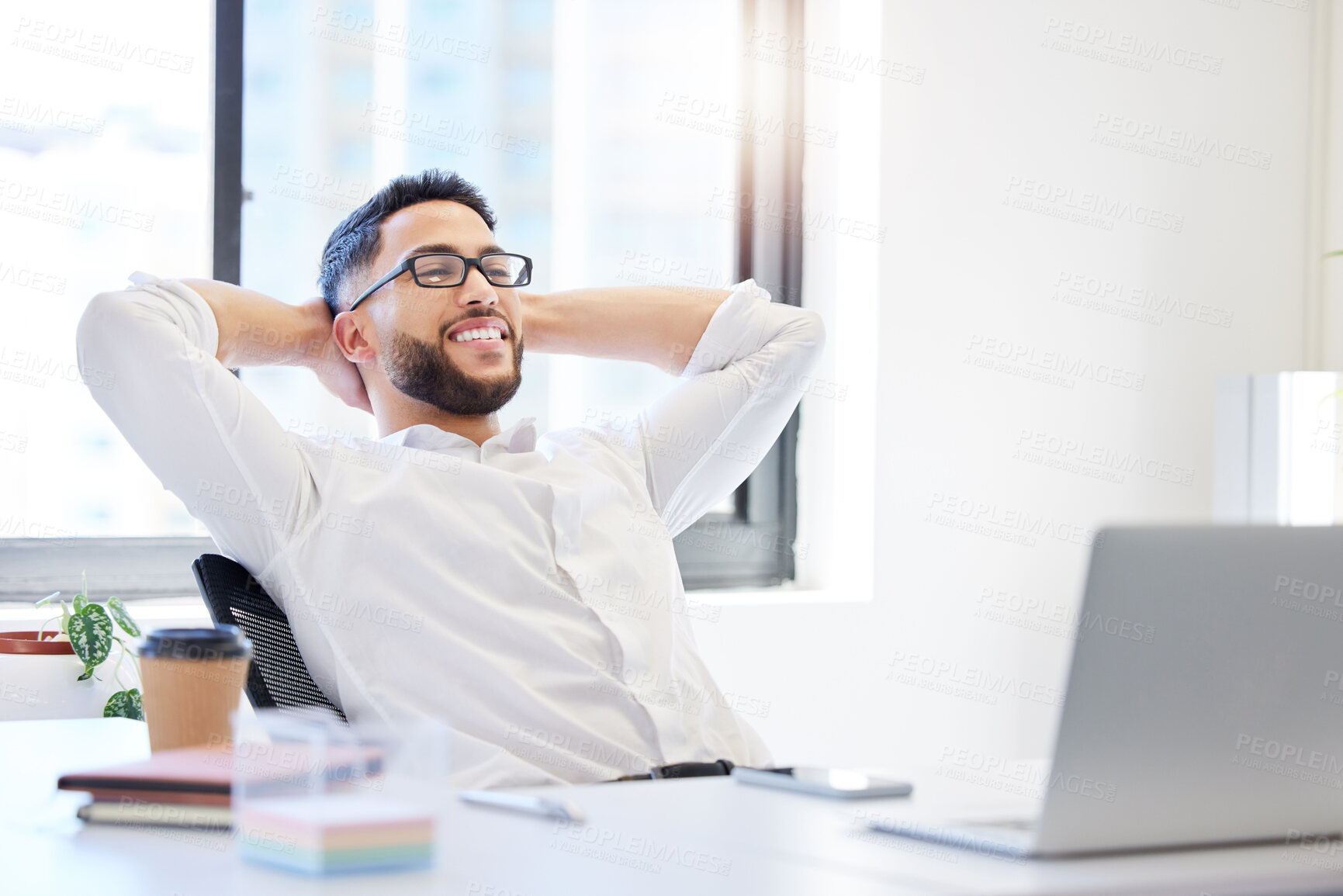 Buy stock photo Shot of a handsome young businessman sitting alone in the office with his hands behind his head and feeling successful