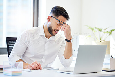Buy stock photo Shot of a handsome young businessman sitting alone in the office and feeling stressed while using his laptop