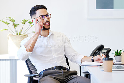 Buy stock photo Shot of a handsome young businessman sitting alone in the office and using his cellphone while writing notes