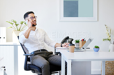 Buy stock photo Shot of a handsome young businessman sitting alone in the office and using his cellphone while writing notes