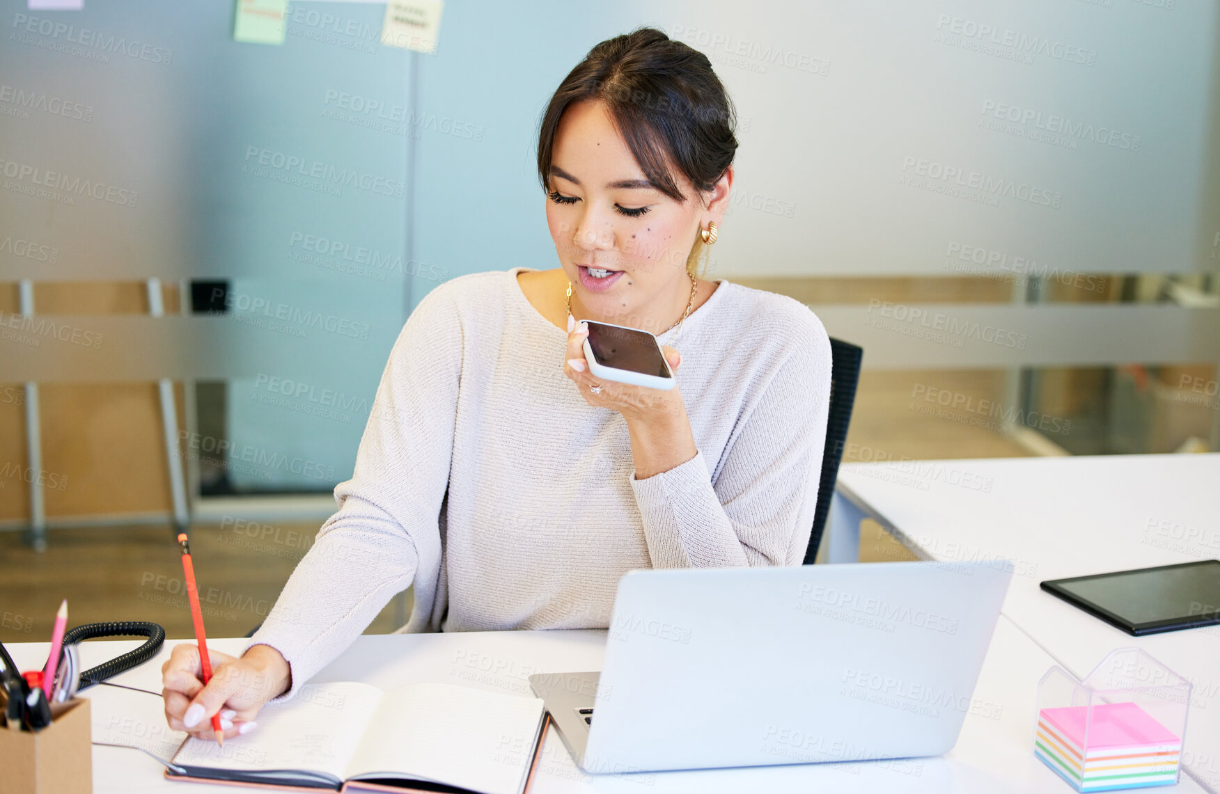 Buy stock photo Shot of an attractive young businesswoman sitting alone in the office and using her cellphone while writing notes