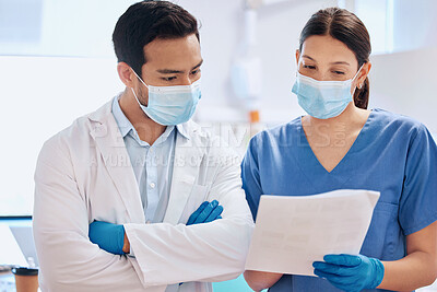 Buy stock photo Shot of a young dentist reading through paperwork with his assistant
