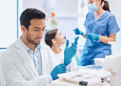 Buy stock photo Shot of a dentist applying his gloves while selecting the tool he needs