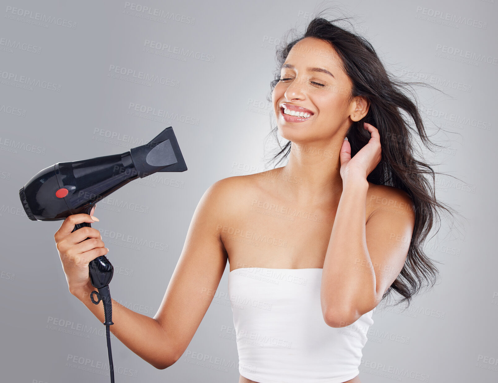 Buy stock photo Cropped shot of an attractive young woman blowdrying her hair against a grey background