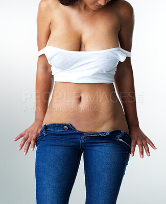 Buy stock photo Studio shot of a sexy young woman taking off her jeans while standing against a grey background