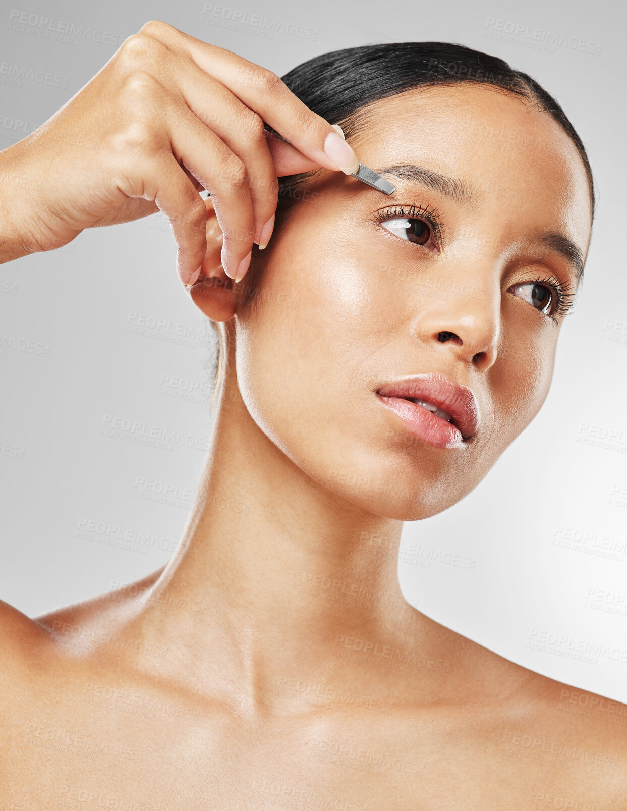 Buy stock photo Studio shot of an attractive young woman tweezing her eyebrows against a grey background