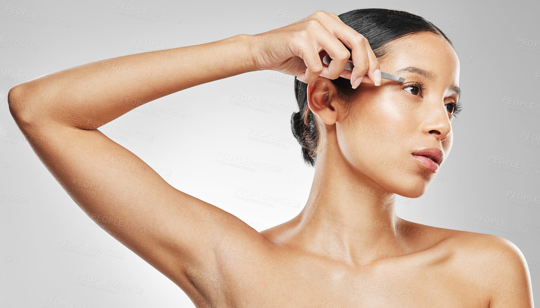 Buy stock photo Studio shot of an attractive young woman tweezing her eyebrows against a grey background