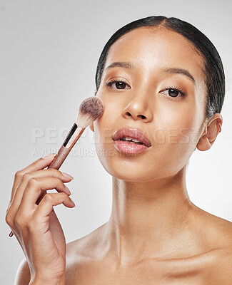 Buy stock photo Studio portrait of an attractive young woman applying makeup to her face with a brush against a grey background