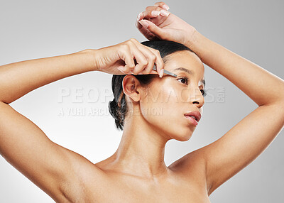 Buy stock photo Studio shot of an attractive young woman tweezing her eyebrows against a grey background