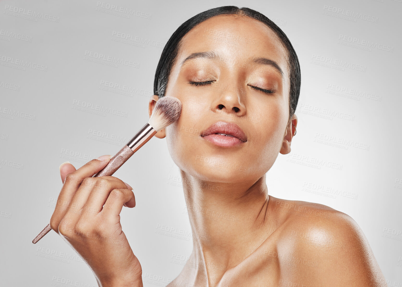 Buy stock photo Studio shot of an attractive young woman applying makeup to her face with a brush against a grey background