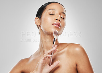 Buy stock photo Studio shot of an attractive young woman applying makeup to her face with a brush against a grey background