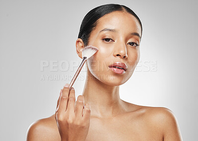 Buy stock photo Studio portrait of an attractive young woman applying makeup to her face with a brush against a grey background