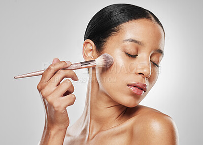 Buy stock photo Studio shot of an attractive young woman applying makeup to her face with a brush against a grey background