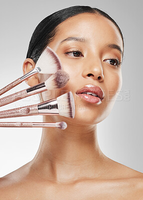 Buy stock photo Studio shot of an attractive young woman holding a collection of makeup brushes against a grey background