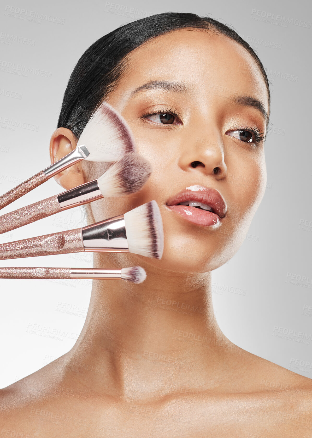 Buy stock photo Studio shot of an attractive young woman holding a collection of makeup brushes against a grey background