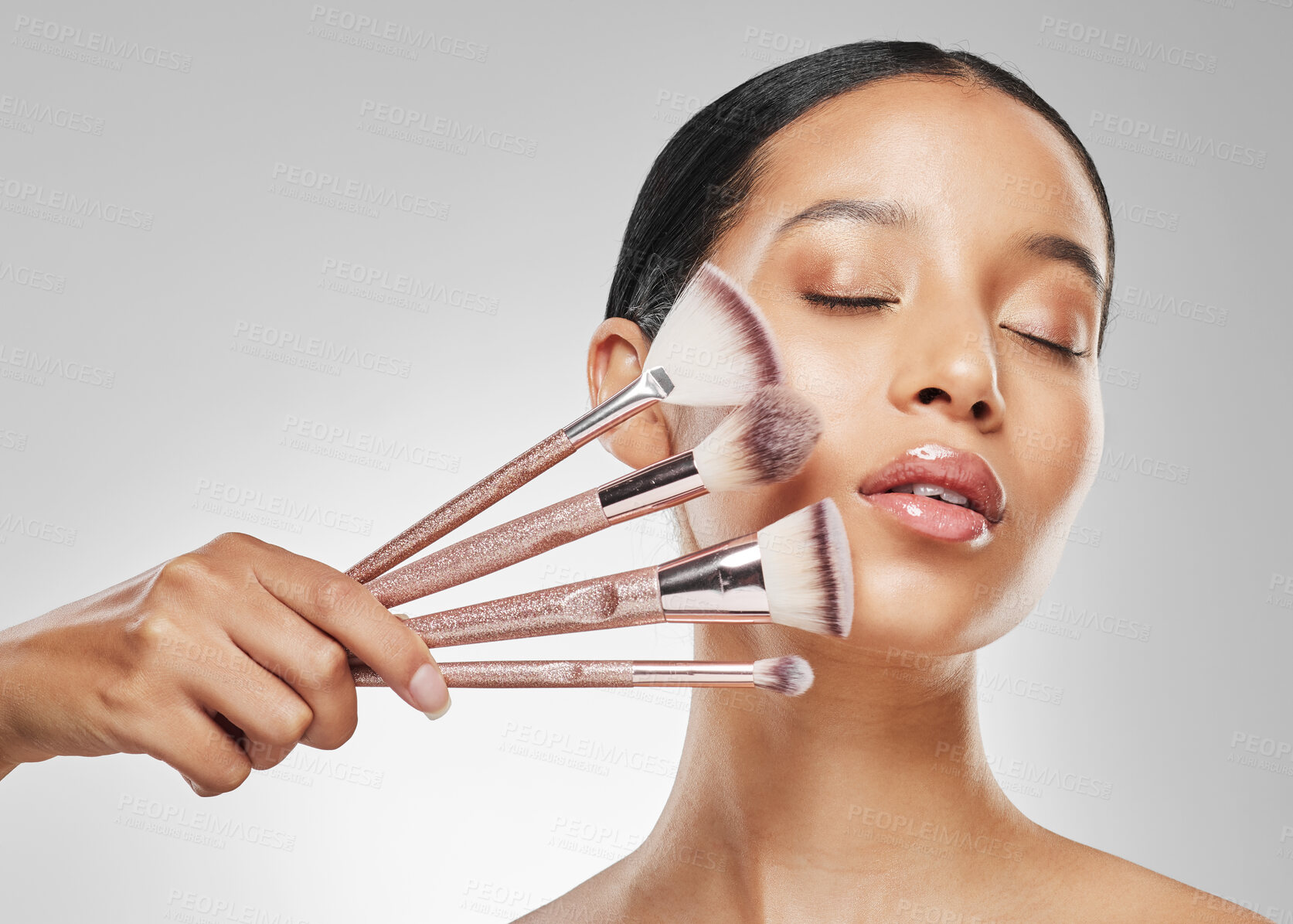 Buy stock photo Studio shot of an attractive young woman holding a collection of makeup brushes against a grey background