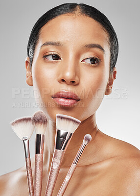 Buy stock photo Studio shot of an attractive young woman holding a collection of makeup brushes against a grey background