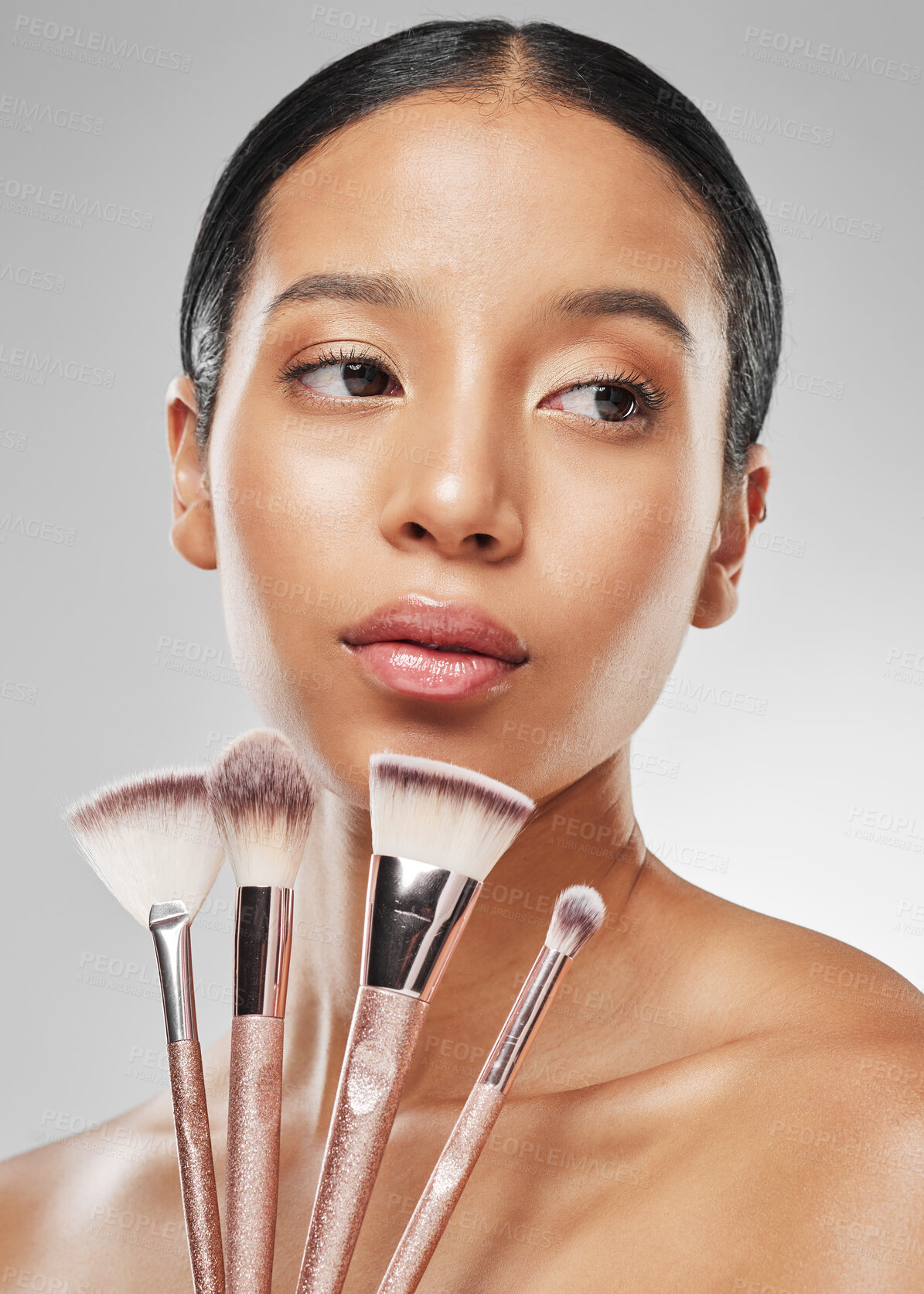 Buy stock photo Studio shot of an attractive young woman holding a collection of makeup brushes against a grey background