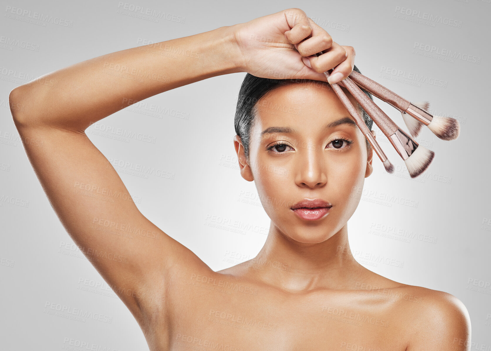 Buy stock photo Studio portrait of an attractive young woman holding a collection of makeup brushes against a grey background